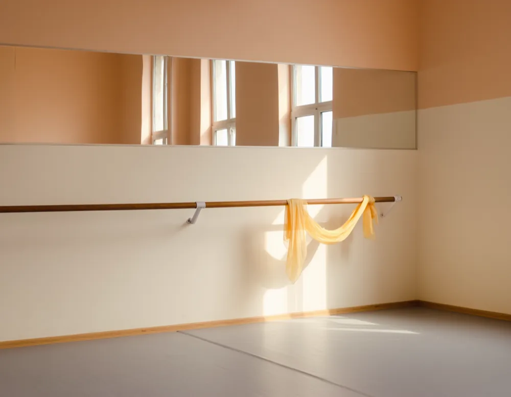 A low wooden ballet barre at child height in front of the studio mirror wall